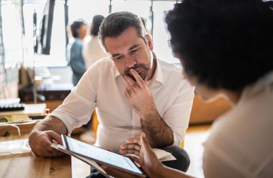A man and woman reviewing papers a tablet device. The man looks deep in thought.